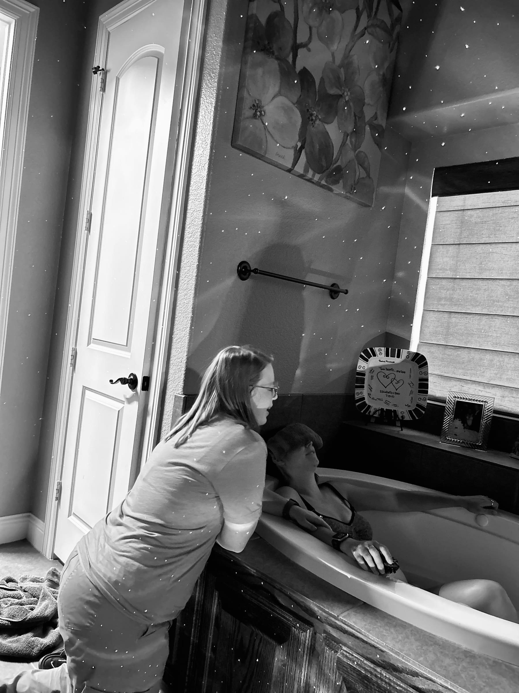 A laboring mother leaning over the edge of a birth tub while Mackenzie supports her